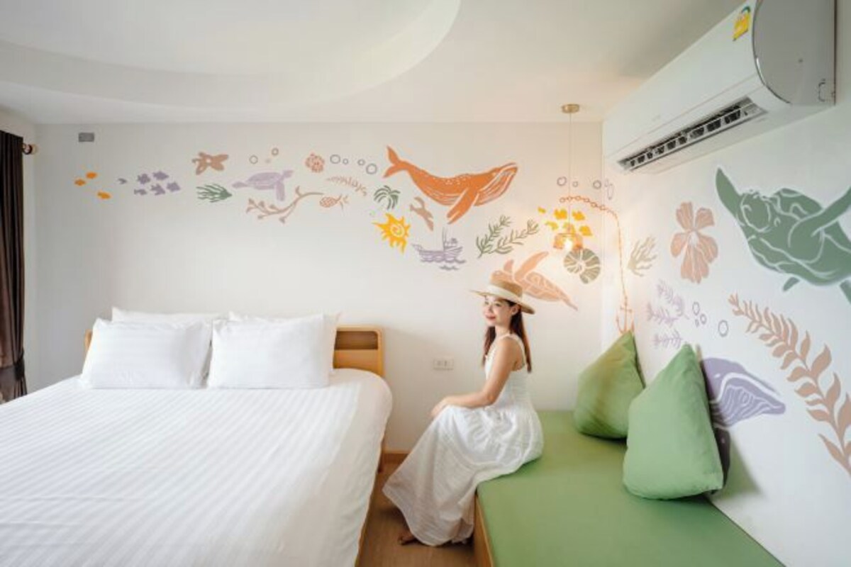 A hotel room with a bed, a green sofa, and a wall decorated with colorful marine life illustrations.