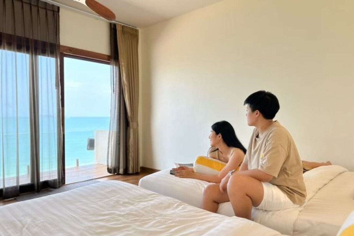 A bedroom with a large window overlooking the sea, a bed, and a bedside table.