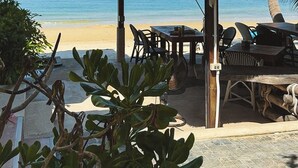 Un restaurante frente a la playa con techo de paja, mesas al aire libre y vistas al océano.