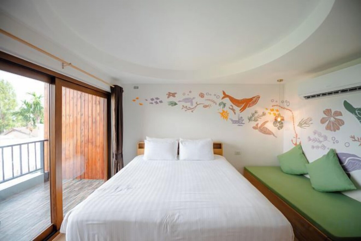 A hotel room with a large bed, a green sofa, and a balcony with wooden flooring.