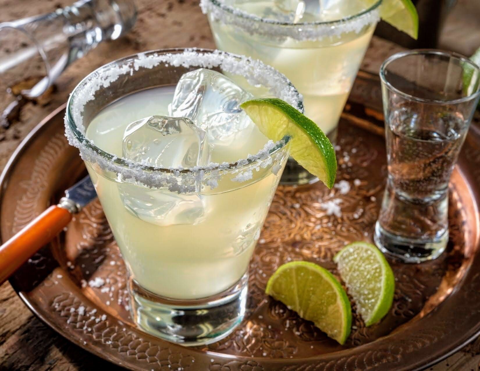 Dos margaritas adornadas con lima sobre una bandeja de cobre.