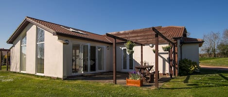 A modern house with a large glass door entrance, a covered patio, and a well-maintained lawn.