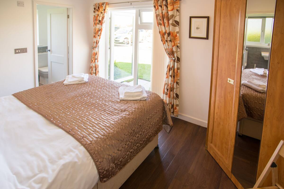 Quarto com uma cama grande, banheiro visível por uma porta aberta e vista para o exterior.