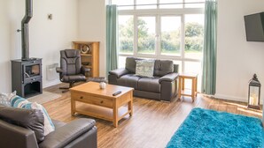 A living room with a fireplace, leather sofas, a coffee table, and a large window with curtains. - Stoneleigh Village (Sidmouth)