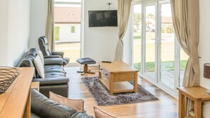 A modern living room with a sofa set, a wooden coffee table, and a TV mounted on the wall. - Stoneleigh Village (Sidmouth)