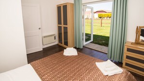 A bedroom with a large bed, a wooden wardrobe, and a sliding glass door leading to a balcony. - Stoneleigh Village (Sidmouth)
