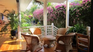 A covered patio with wicker furniture, a white fence, and lush greenery. - La Posada Azul (San Juan del Sur)