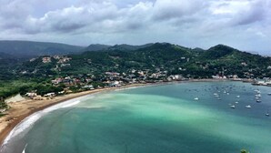 A coastal landscape with a beach, clear turquoise waters, and a town in the background. - La Posada Azul (San Juan del Sur)