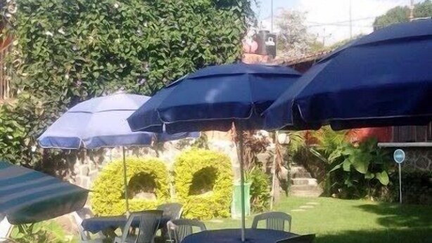 Un área de patio al aire libre con varias mesas y sillas, cubierta por sombrillas azules.