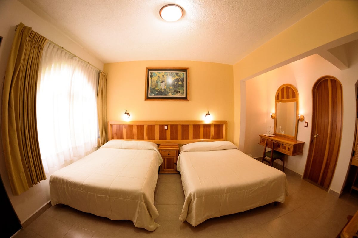 A hotel room with two beds, a wooden headboard, a desk with a mirror, and a painting on the wall.