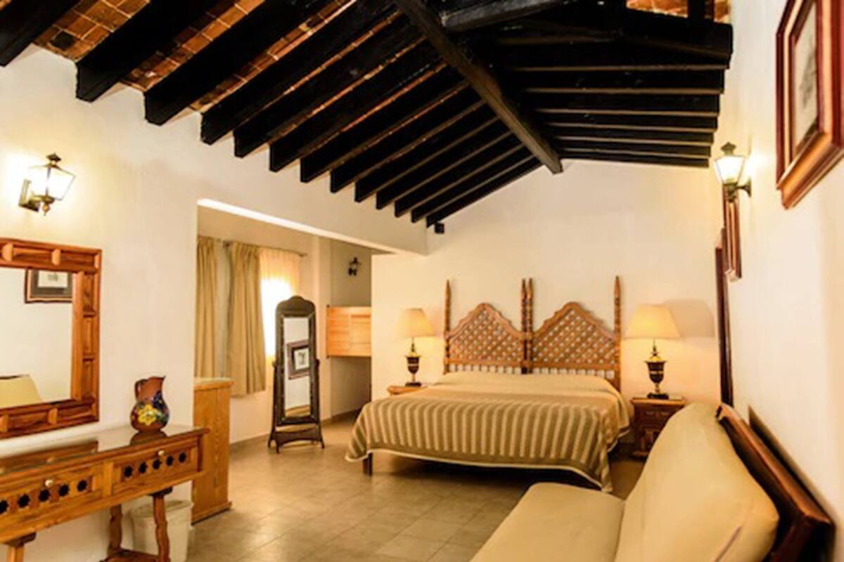 A bedroom with a wooden ceiling, a bed with a patterned headboard, bedside lamps, and a wooden dresser.