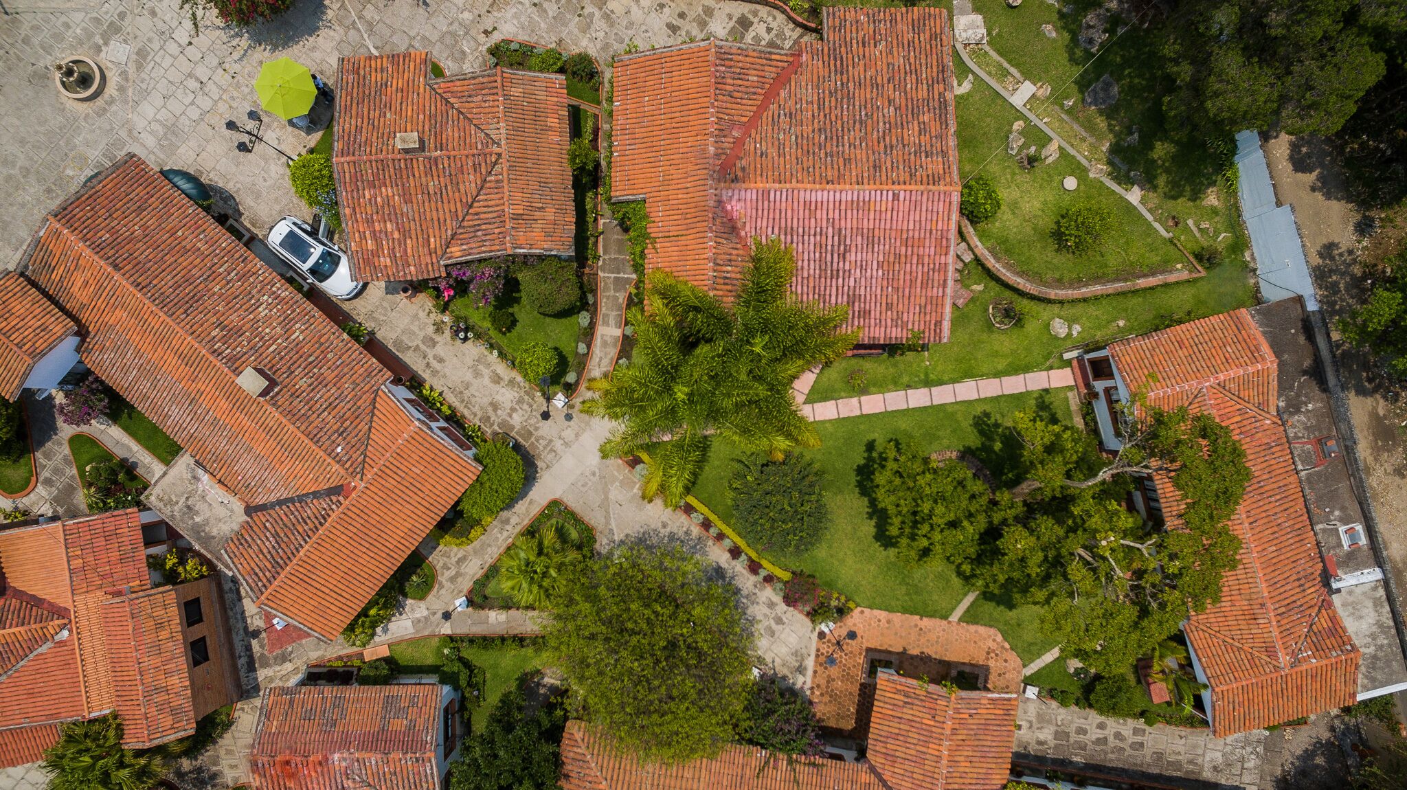 Vista aérea de una zona residencial con casas de tejados de terracota, un camino central y vegetación circundante.