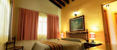 A hotel room with a bed, two bedside lamps, a window with curtains, a painting on the wall, and a mirror.