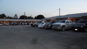 A parking lot with several vehicles, including a white pickup truck and a black SUV, in front of a building with a flat roof. - A OK Motel (Muenster)