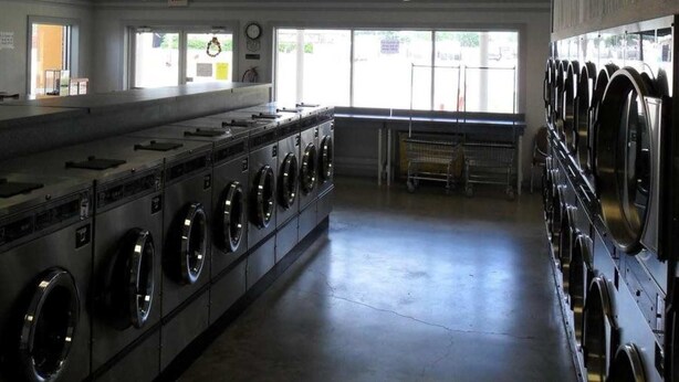 A laundry facility with multiple washing machines and dryers, a long counter, and large windows allowing natural light. - A OK Motel (Muenster)