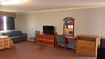 Ein Hotelzimmer mit einem Bett, einem Sofa, einem Schreibtisch mit Fernseher, einem Spiegel und einer Kommode.