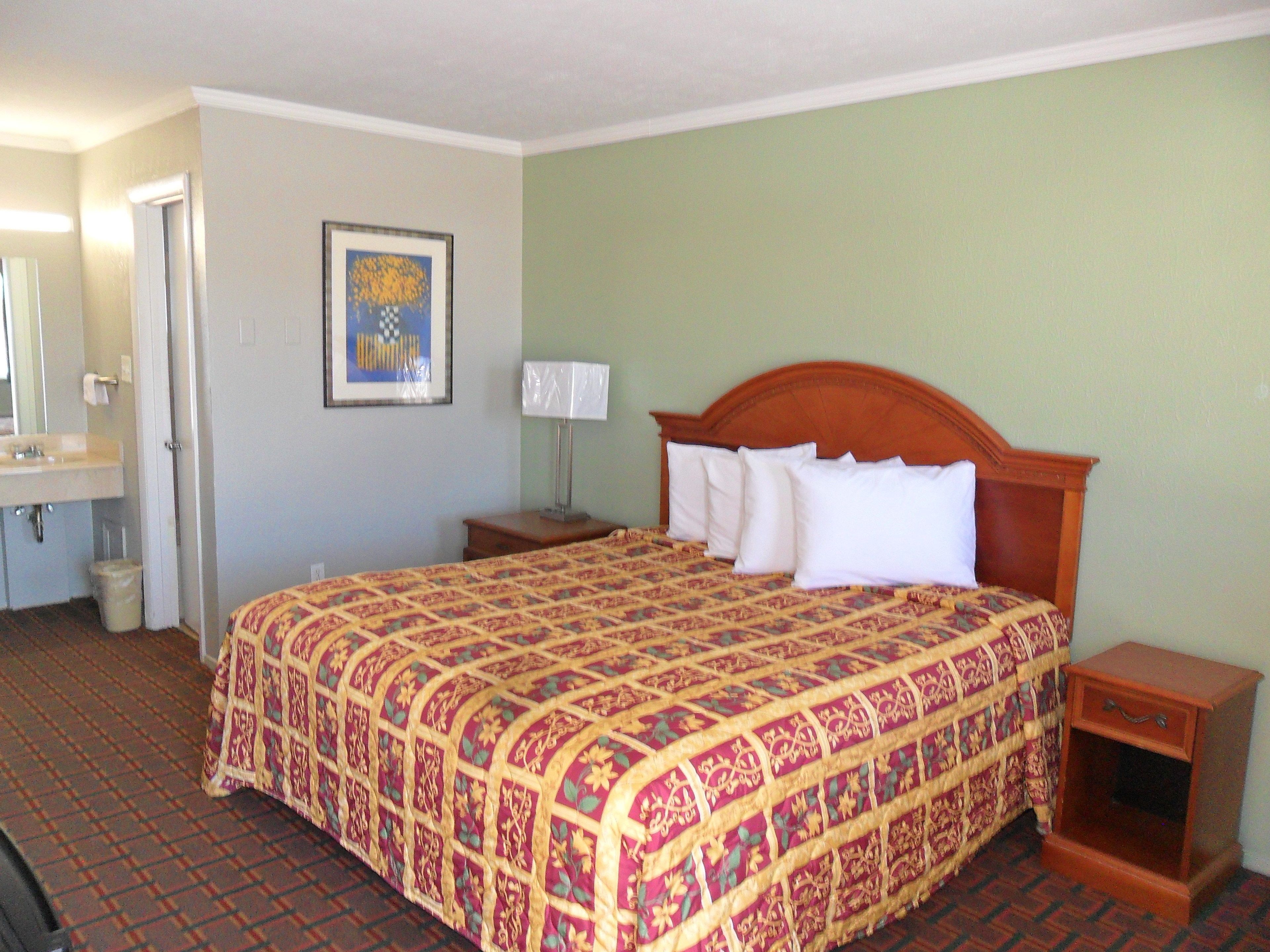 A hotel room with a large bed, a bedside table, a nightstand, a mirror, and a framed picture on the wall.