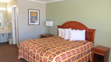 A hotel room with a large bed, a bedside table, a nightstand, a mirror, and a framed picture on the wall.
