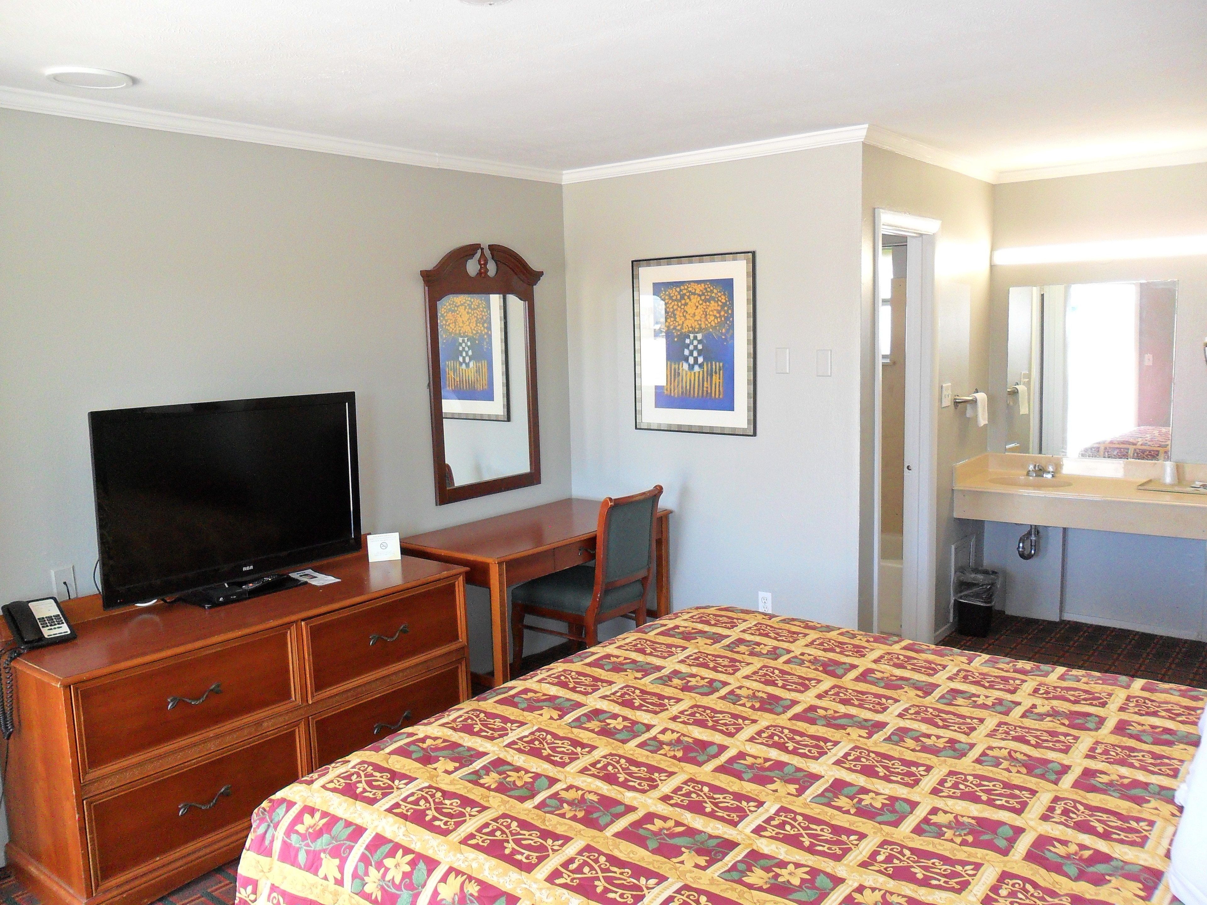 A hotel room with a bed, a desk, a television, a dresser, and a bathroom.