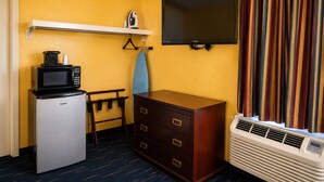 A compact hotel room with a kitchenette, a flat-screen TV, a wooden dresser, a bench, and a window with curtains. - Country Inn Sterling (Sterling)