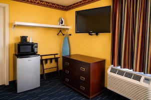 Habitación de hotel compacta con kitchenette, un televisor de pantalla plana, cómoda de madera, una banca y ventana con cortinas.