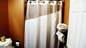 A bathroom with a shower curtain, a towel rack with towels, a toilet, and a soap dispenser. - Country Inn Sterling (Sterling)