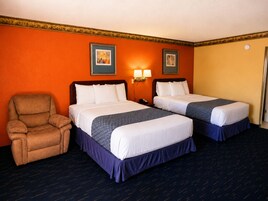 Quarto de hotel com duas camas, uma cadeira e duas luminárias fixadas na parede.