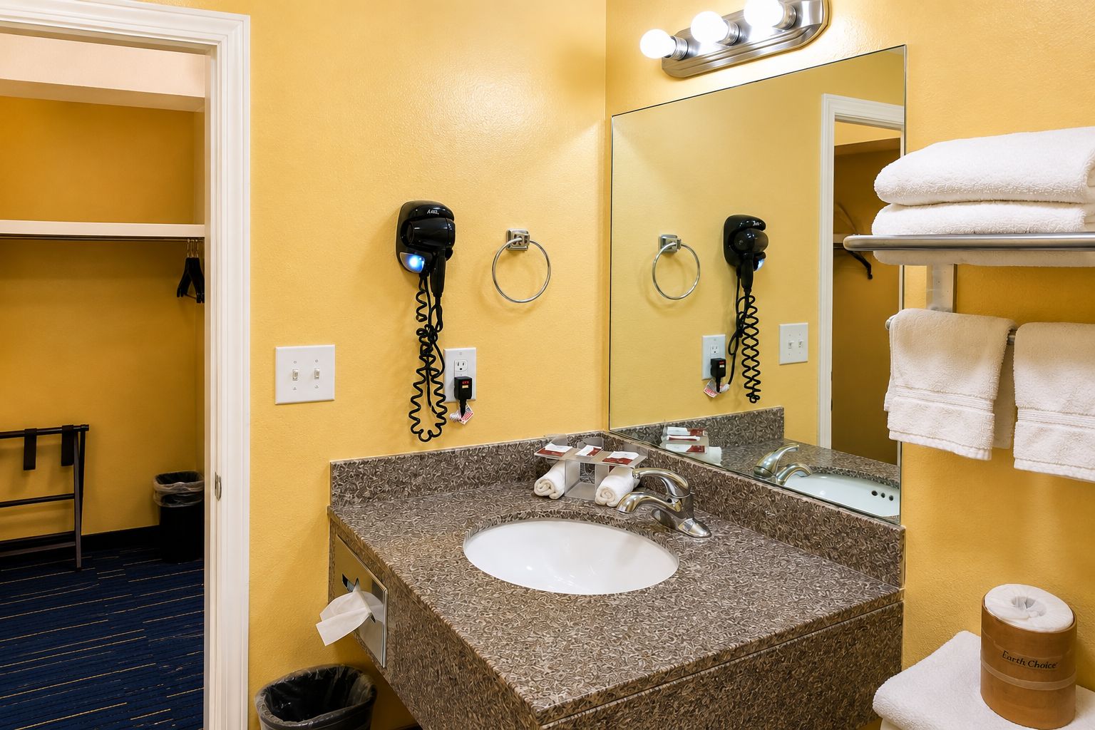 Casa de banho de hotel com lavatório de granito, dois secadores de cabelo, um porta-toalhas e um espelho.