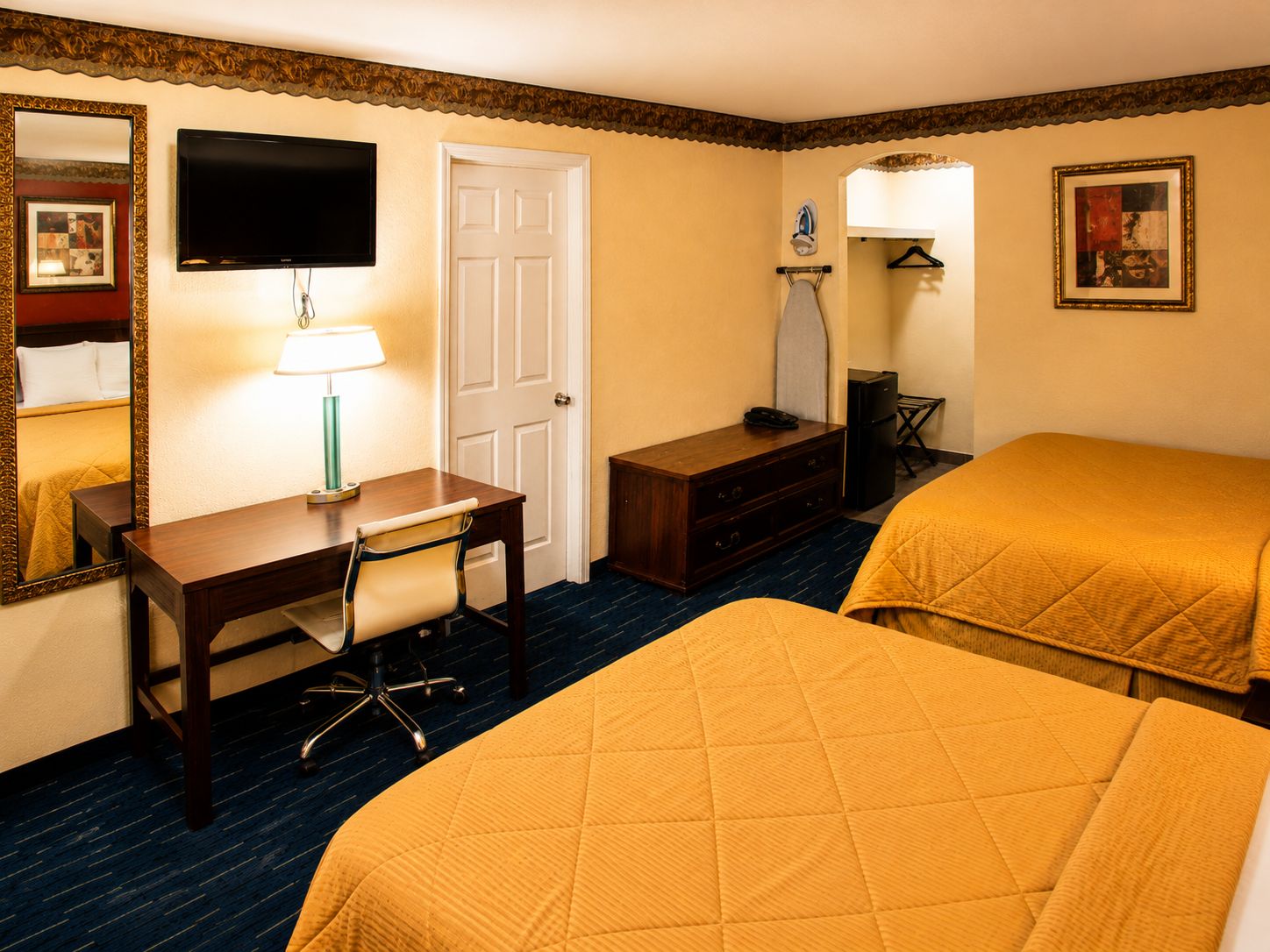 A hotel room with two beds, a desk with a chair, a television, a door, and a mirror.
