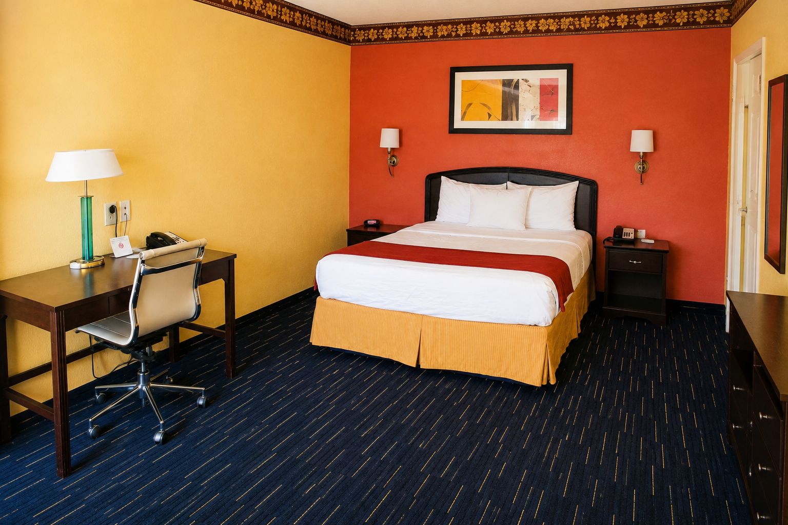 Ein Hotelzimmer mit Bett, Schreibtisch, Stuhl und zwei Nachttischen.