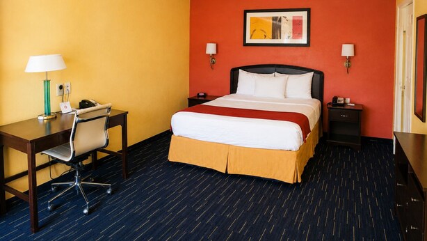 A hotel room with a bed, desk, chair, and two bedside tables. - Country Inn Sterling (Sterling)