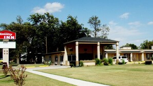 A Country Inn with a covered outdoor seating area, a sign indicating it's open, and a parking lot with a white van. - Country Inn Sterling (Sterling)