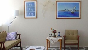 Una sala de estar con sofá, sillón, televisor y cuadros en la pared.