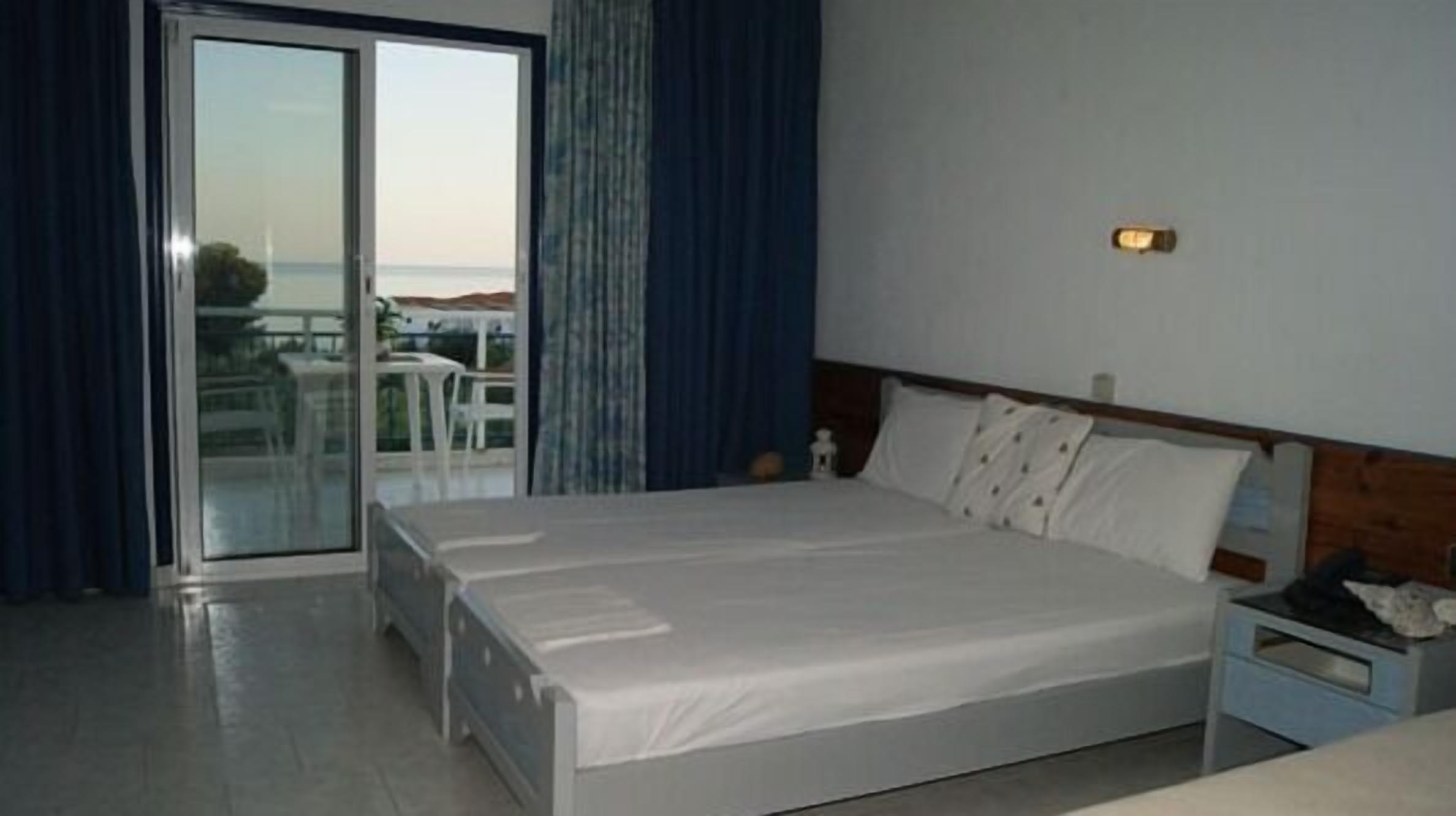 A hotel room with a bed, a nightstand, a window with curtains, and a view of the outdoors.