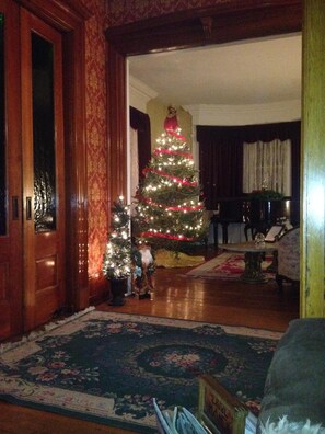A traditional living room with a large Christmas tree, a piano, and a small table. - Victorian Charm Inn (Towanda)