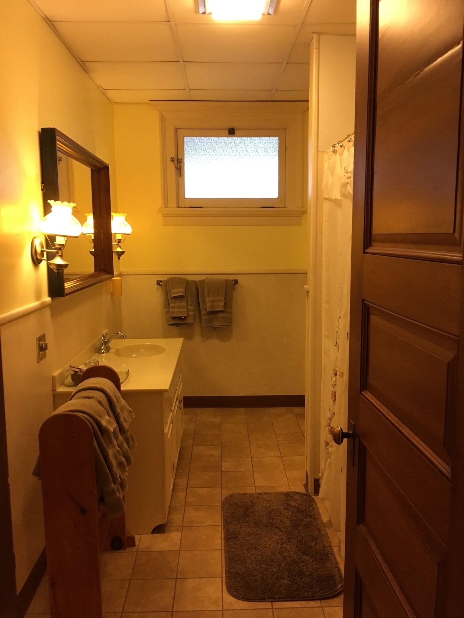 A bathroom with a sink, mirror, and window. There is a towel rack with towels and a rug on the floor.