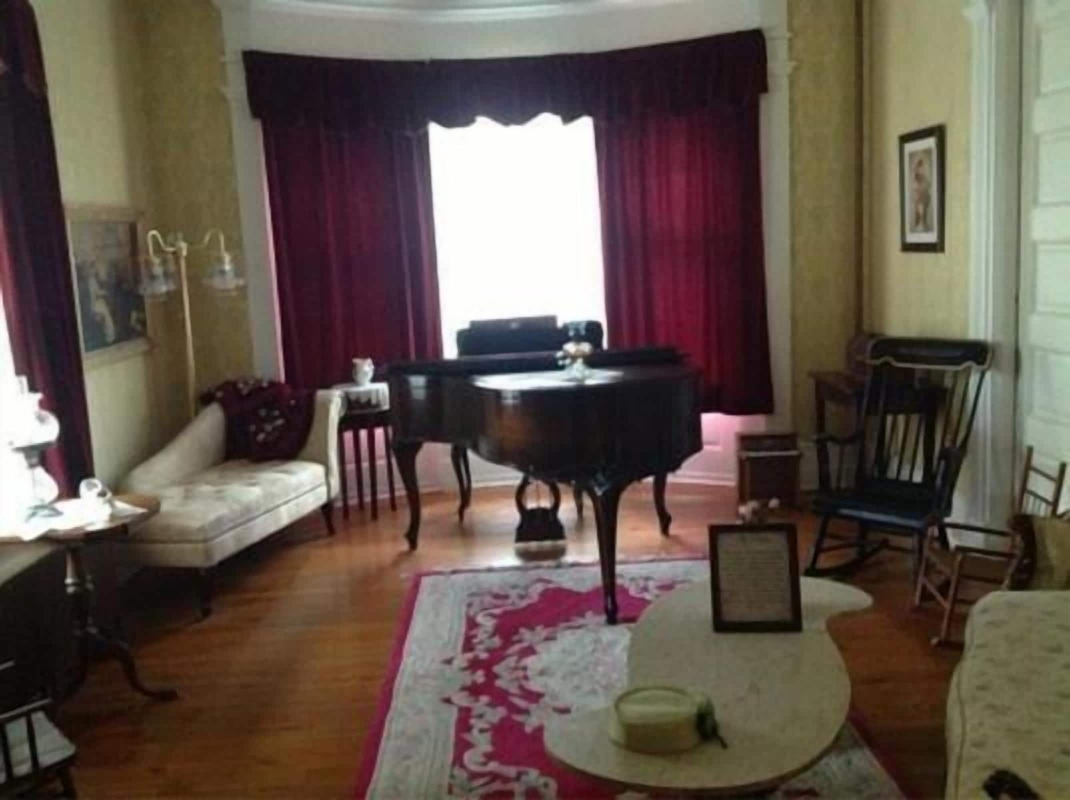 A room with a piano, a sofa, a table with a candle, and a patterned rug.