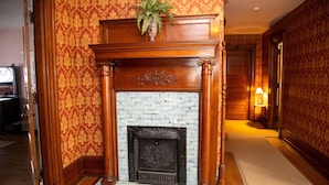 A fireplace with a brick surround and ornate wood mantel, set in a room with patterned wallpaper and wooden flooring. - Victorian Charm Inn (Towanda)