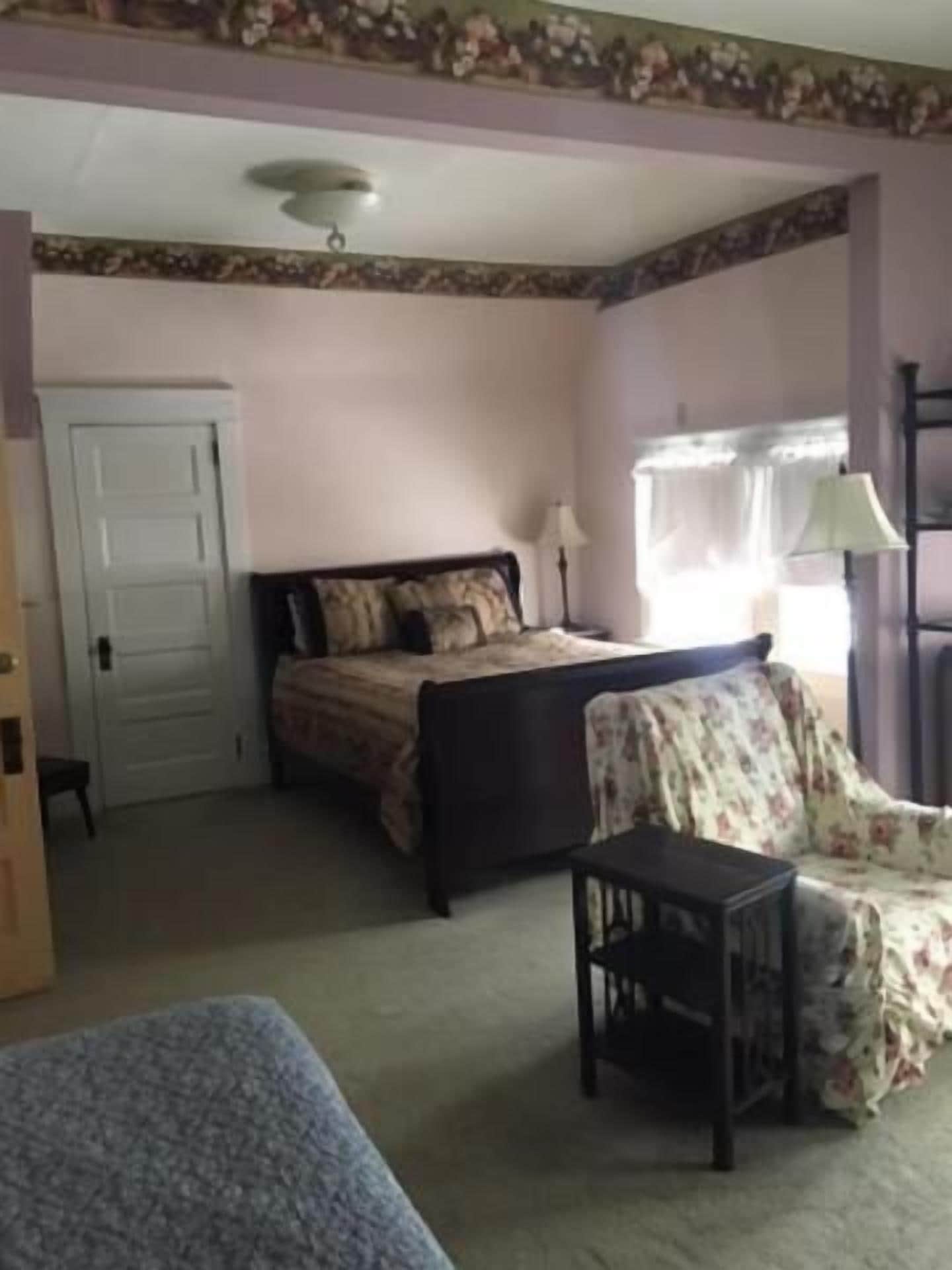 A bedroom with a bed, a chair, a table, and a wardrobe.