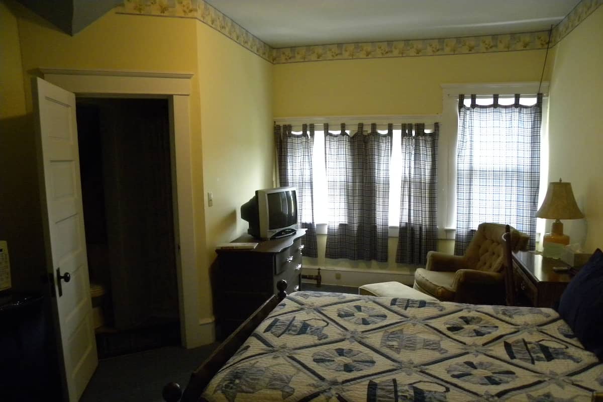 A bedroom with a bed, a chair, a desk, a television, and a window with curtains.