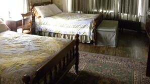 A bedroom with two beds, a wooden headboard, a nightstand, a dresser, a window with curtains, and a patterned rug.