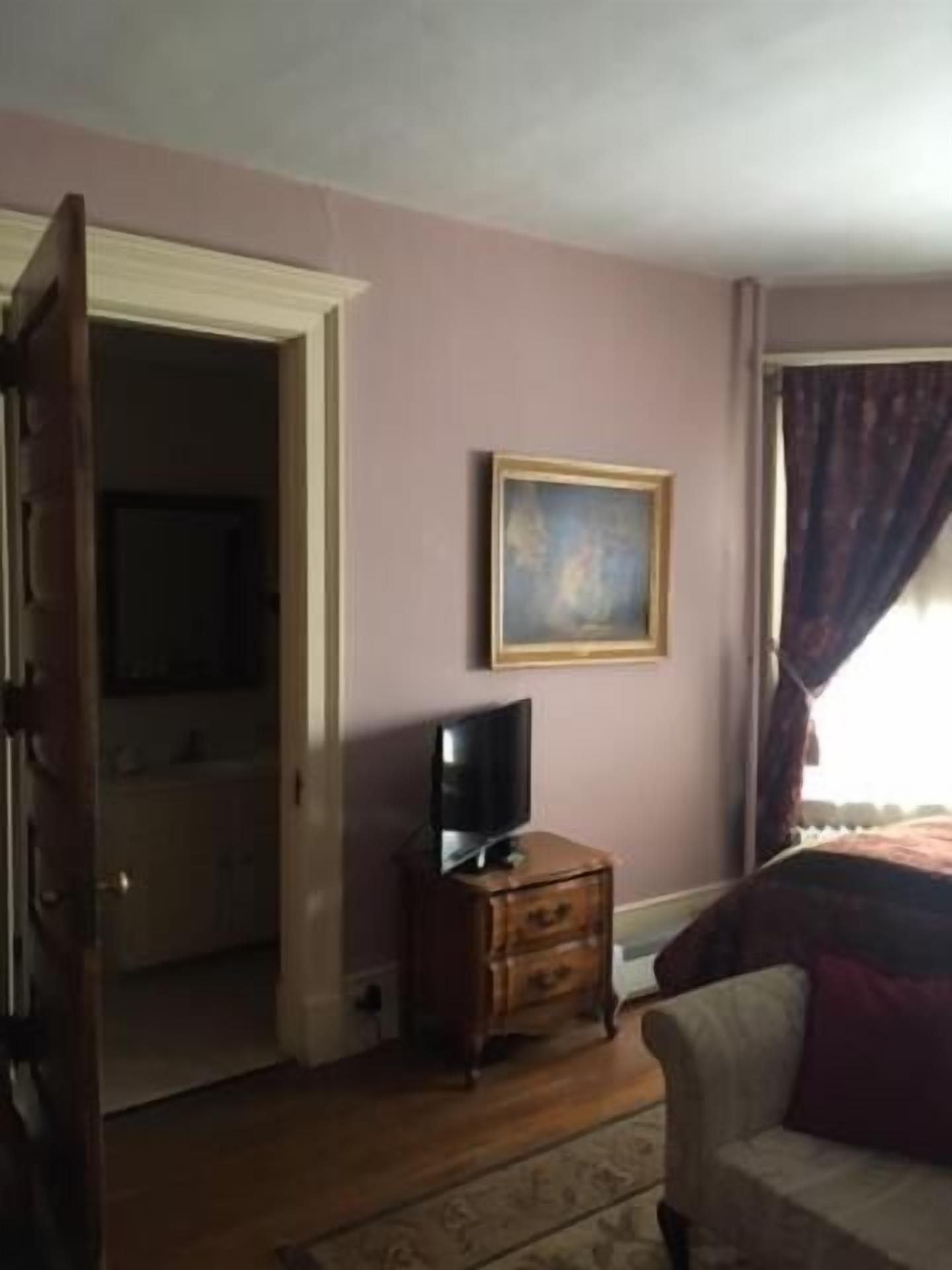Una habitación con un aparador de madera, un televisor encima, un cuadro en la pared y una ventana con cortinas.