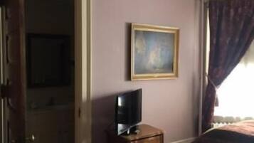Una habitación con un aparador de madera, un televisor encima, un cuadro en la pared y una ventana con cortinas.