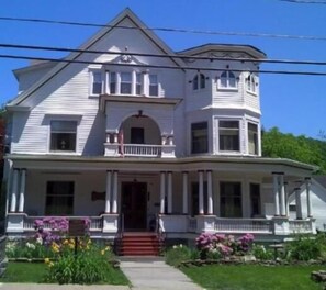 A two-story house with a central entrance, a porch with columns, and a small front yard with flowers.