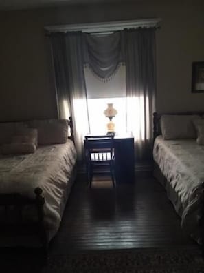 A room with two single beds, a small table with a lamp, and a window with curtains.