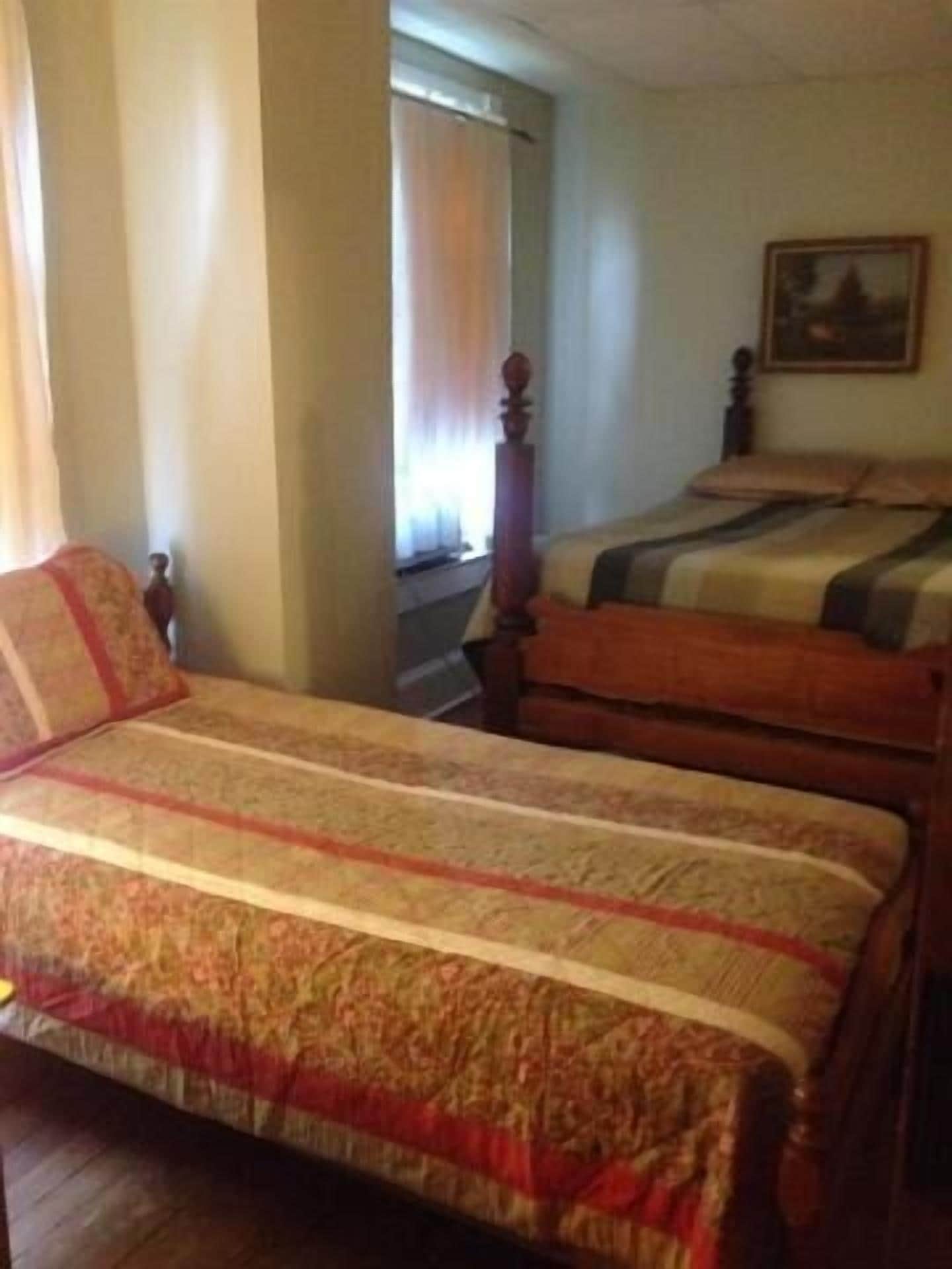 A room with two beds, a window with curtains, and a painting on the wall.