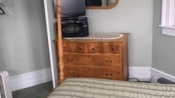 A bedroom with a bed, a wooden dresser, a television, and a mirror.
