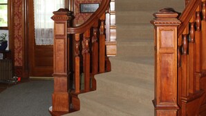 A grand wooden staircase with intricate balusters, leading to a landing with a potted plant. - Victorian Charm Inn (Towanda)