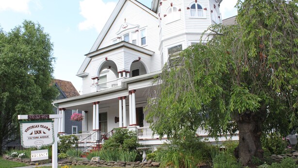 A Victorian Charm Inn with a white facade, multiple balconies, and a stone garden. - Victorian Charm Inn (Towanda)