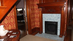 A room with a fireplace, a wooden table with a vase and photographs, and patterned wallpaper. - Victorian Charm Inn (Towanda)